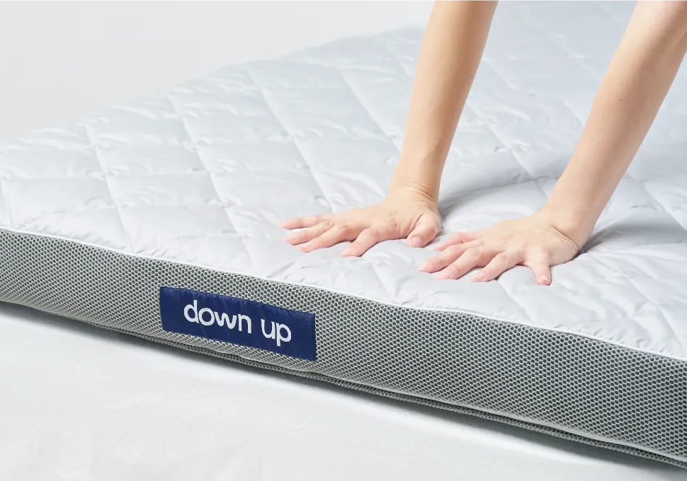 down up のロゴが付いたマットレスを手で押した様子